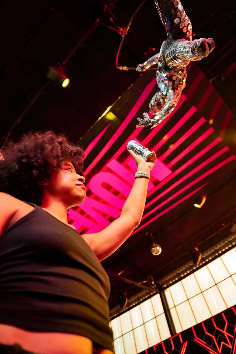 A guest raises an Extreme can toward an aerial performer suspended above the floor, against the pink EXTREME backdrop